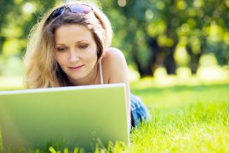 Woman lying in a meadow with a laptop and working.