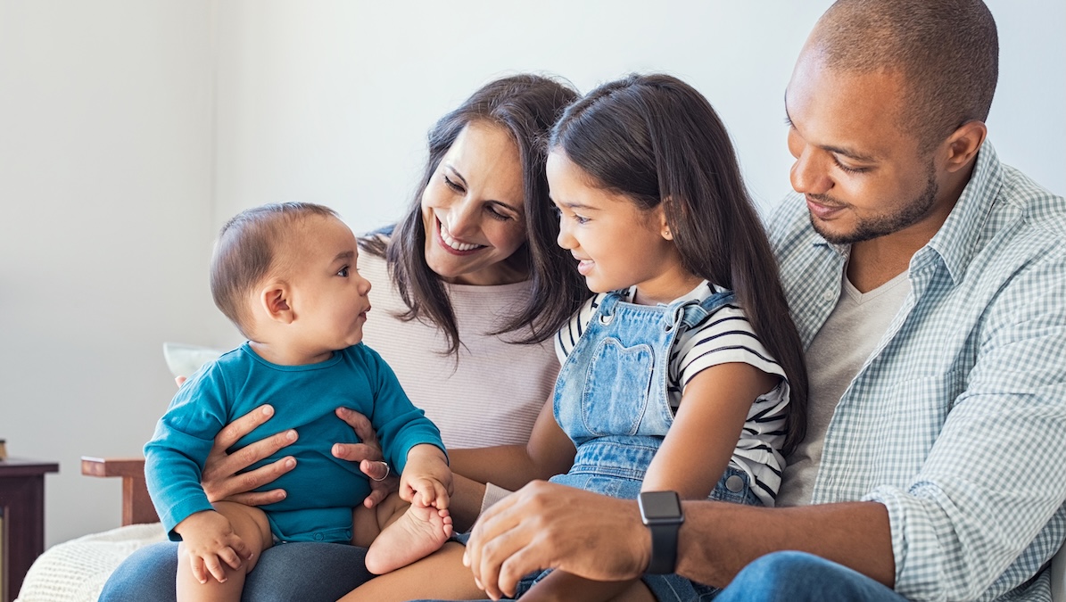 Eltern sitzen mit ihren zwei Kleinkindern lachend auf dem Sofa